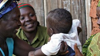 Three women in Sub-Saharan Africa laugh with a baby.